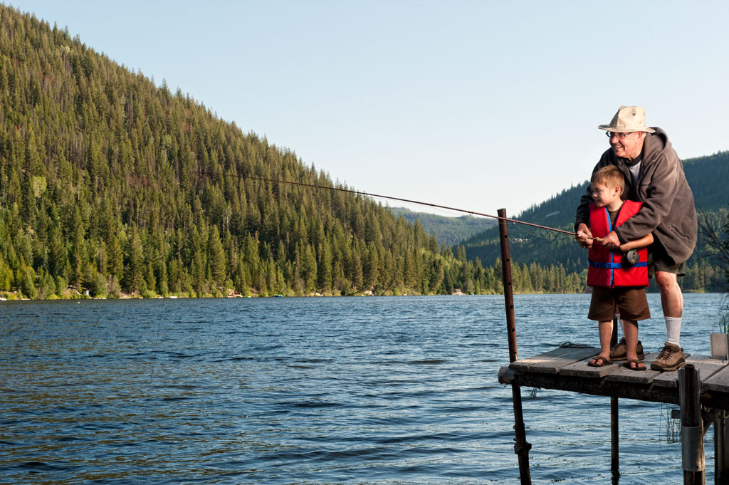 a granfather teaching his grandchild to fish off a dock