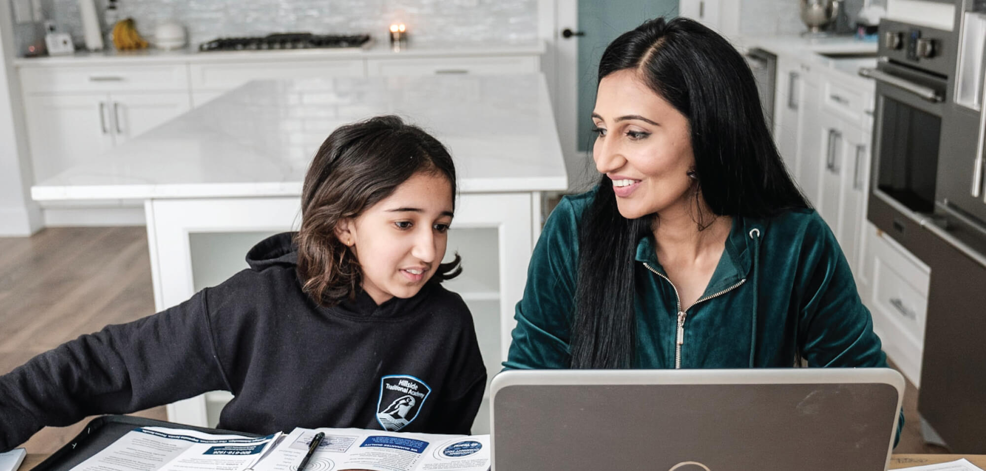 a mother and her a preteen child chatting while using a laptop