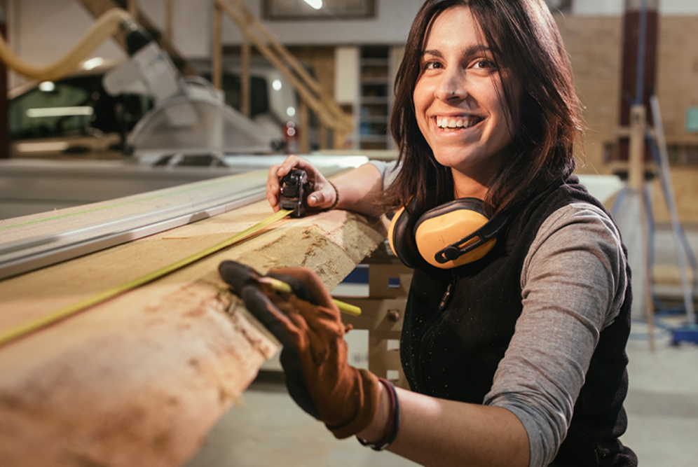 tradeswoman using measuring tape on lumber