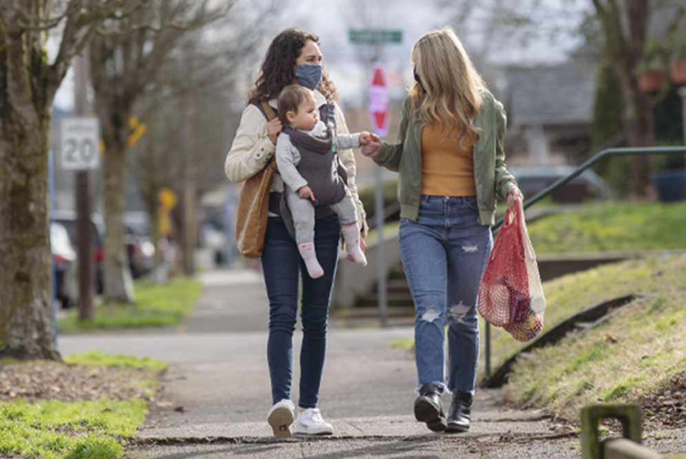 two women walking in a neighborhood with a baby strapped onto one woman's front